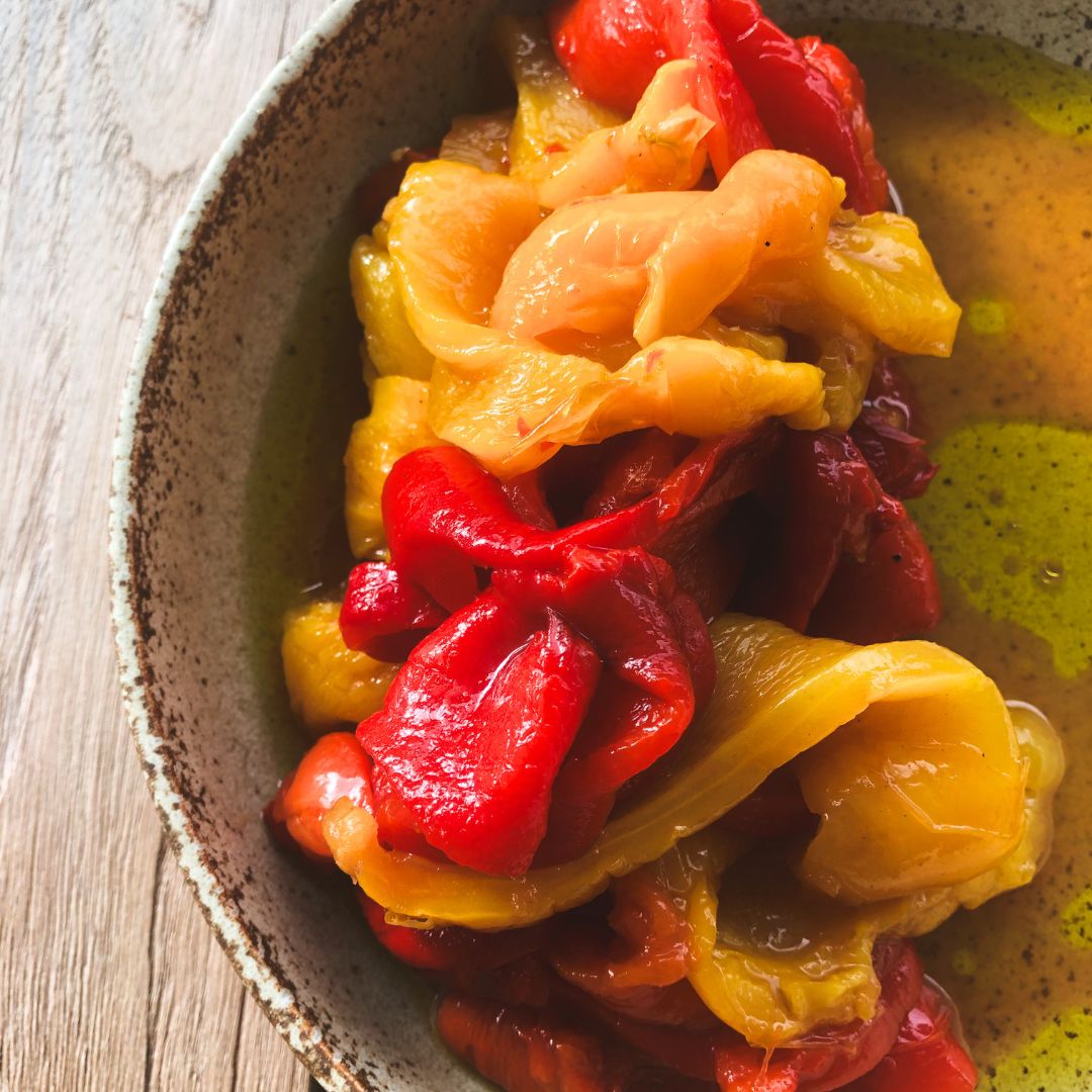 Roasted and marinated red and yellow capsicums resting, in their juices, on a rustic serving plate.